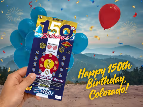 A hand holds up a $5 Colorado Lottery scratch-off ticket titled "150th Birthday!" against a festive background celebrating Colorado's sesquicentennial. The ticket is dark blue and features the Colorado state flag design with dollar signs in place of the usual layout, along with a "Winning Numbers" section and an "ESTD 1876 BONUS" spot.